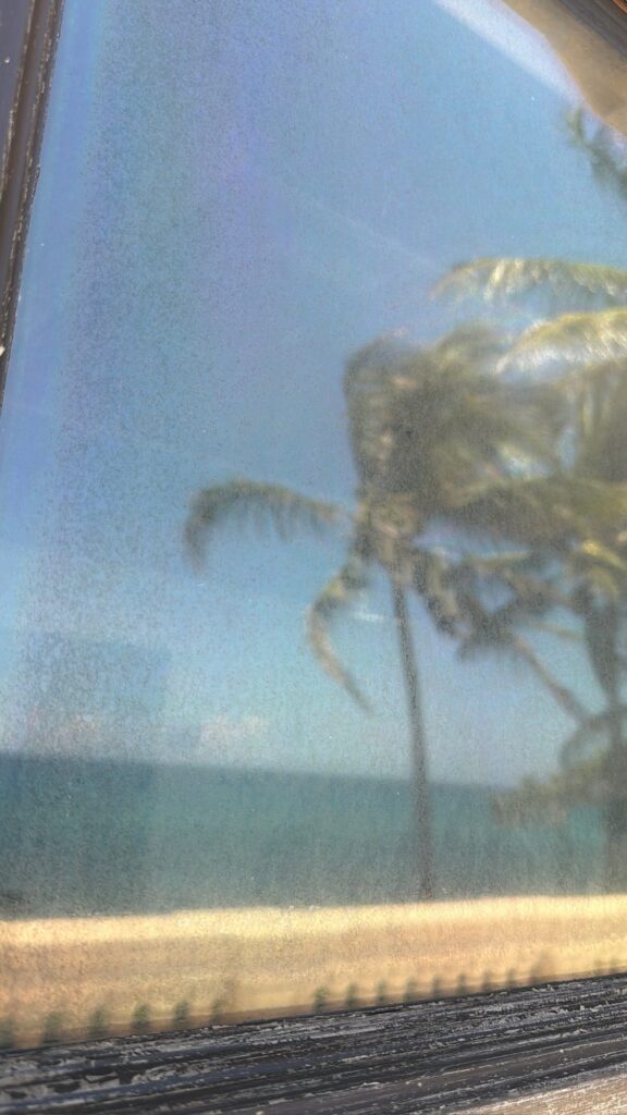 Close-up of spotted window glass with the ocean behind it before restoration in Jupiter, FL